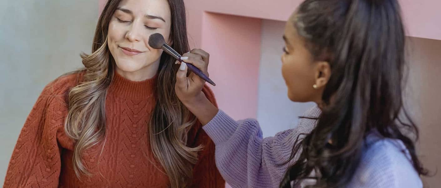 young ethnic lady applying foundation on face of friend with brush