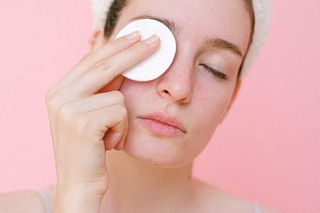 woman removing eye makeup with cotton pad