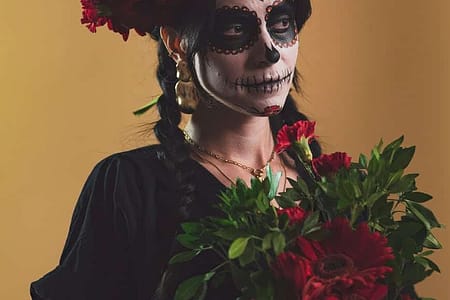 woman in catrina makeup holding a bouquet of red flowers