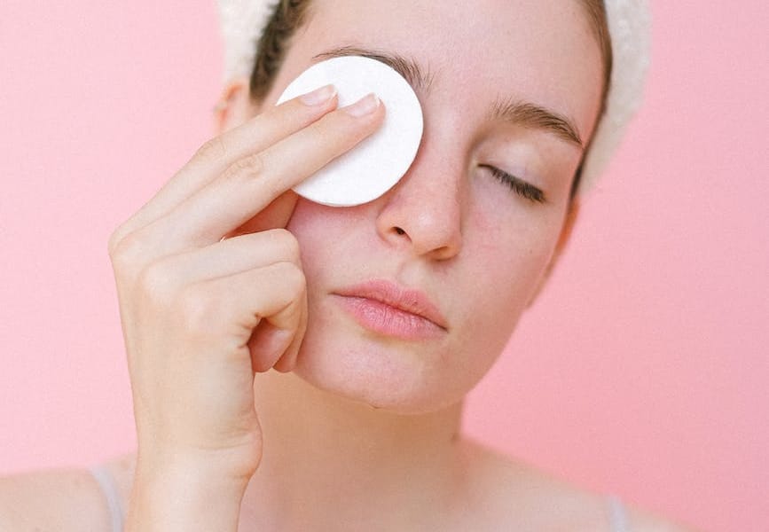 woman removing eye makeup with cotton pad