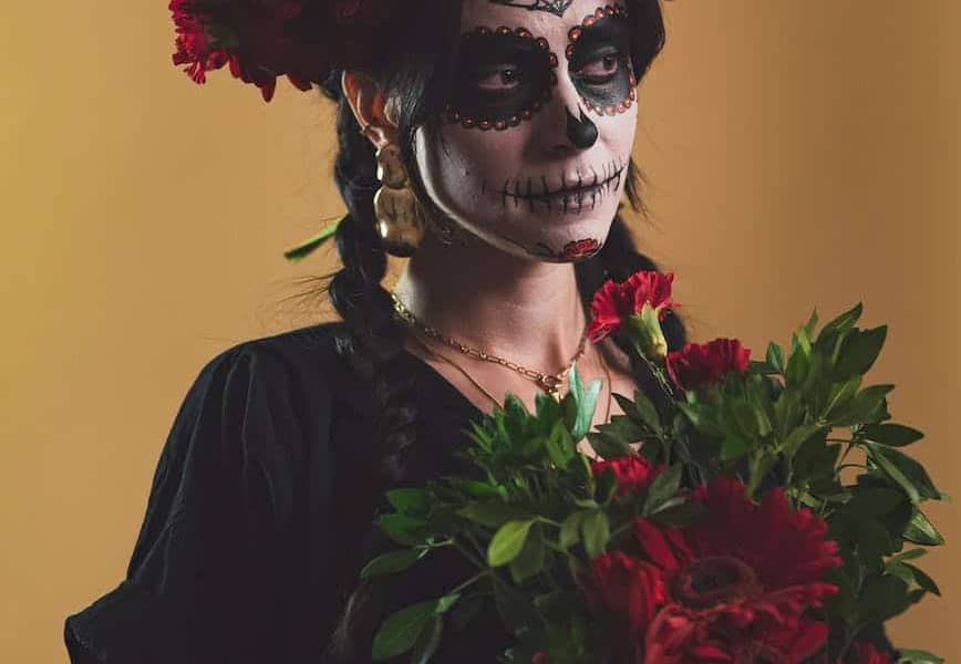 woman in catrina makeup holding a bouquet of red flowers