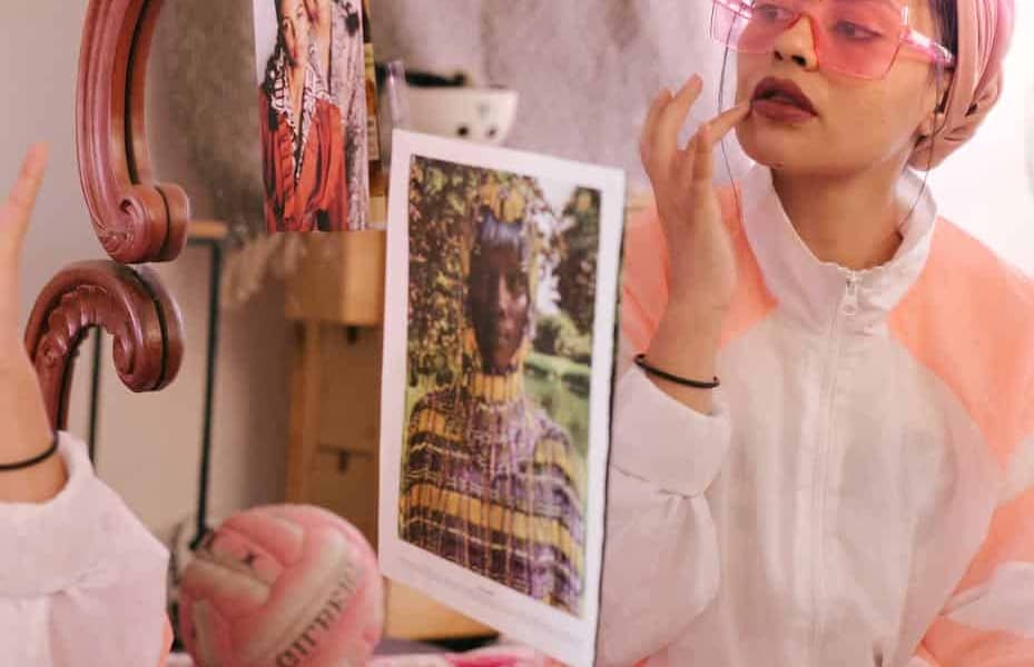 trendy ethnic woman applying lip balm in front of mirror